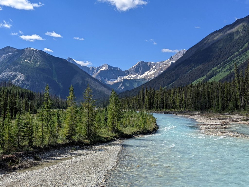 View of bright blue river with giant rocky mountains off in the distance